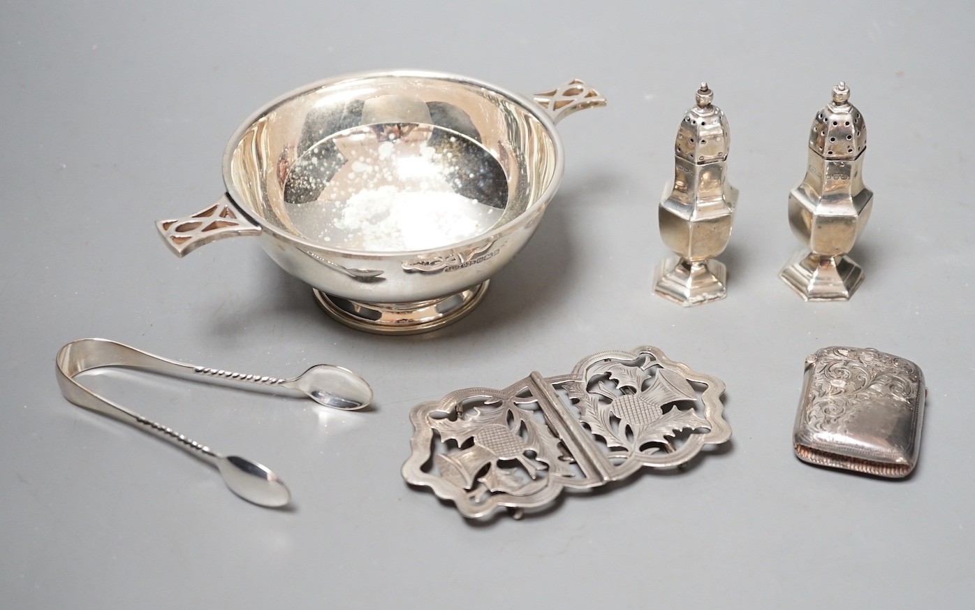 A group of assorted small silver, including a modern two handled bowl, pepperettes, vest case, belt buckle and tongs.